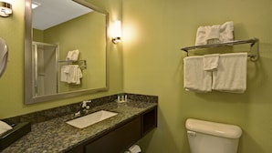 A bathroom with a granite countertop sink, a mirror, a towel rack with towels, and a toilet.