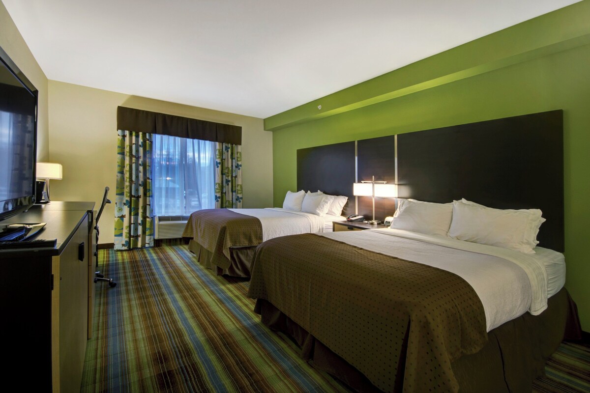 A hotel room with two beds, a desk, a TV, and a window with curtains.