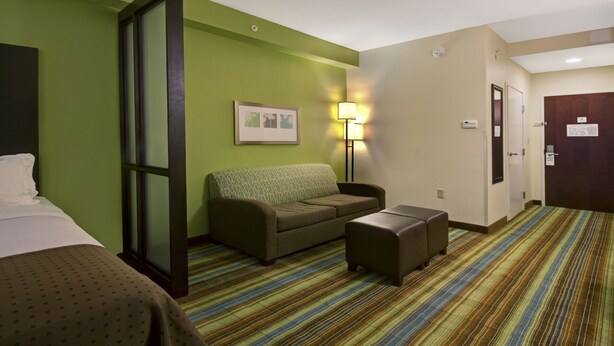 A hotel room with a bed, a sofa, a small table, a lamp, and a striped carpet.