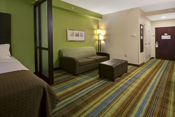 A hotel room with a bed, a sofa, a small table, a lamp, and a striped carpet.