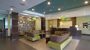Vestíbulo de hotel con una mesa de recepción, zona de estar con sofás y una pared decorada con espejos circulares.