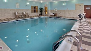 Una piscina interior con agua cristalina, un flotador salvavidas y un cartel con las normas de la piscina.