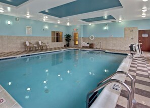 An indoor swimming pool with clear water, a lifebuoy, and a pool rule sign.