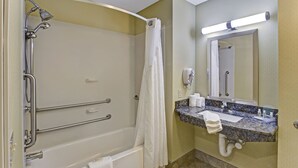 A bathroom with a bathtub, shower, grab bars, a sink with a marble countertop, and a mirror.