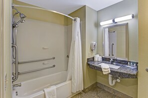 A bathroom with a bathtub, shower, grab bars, a sink with a marble countertop, and a mirror.