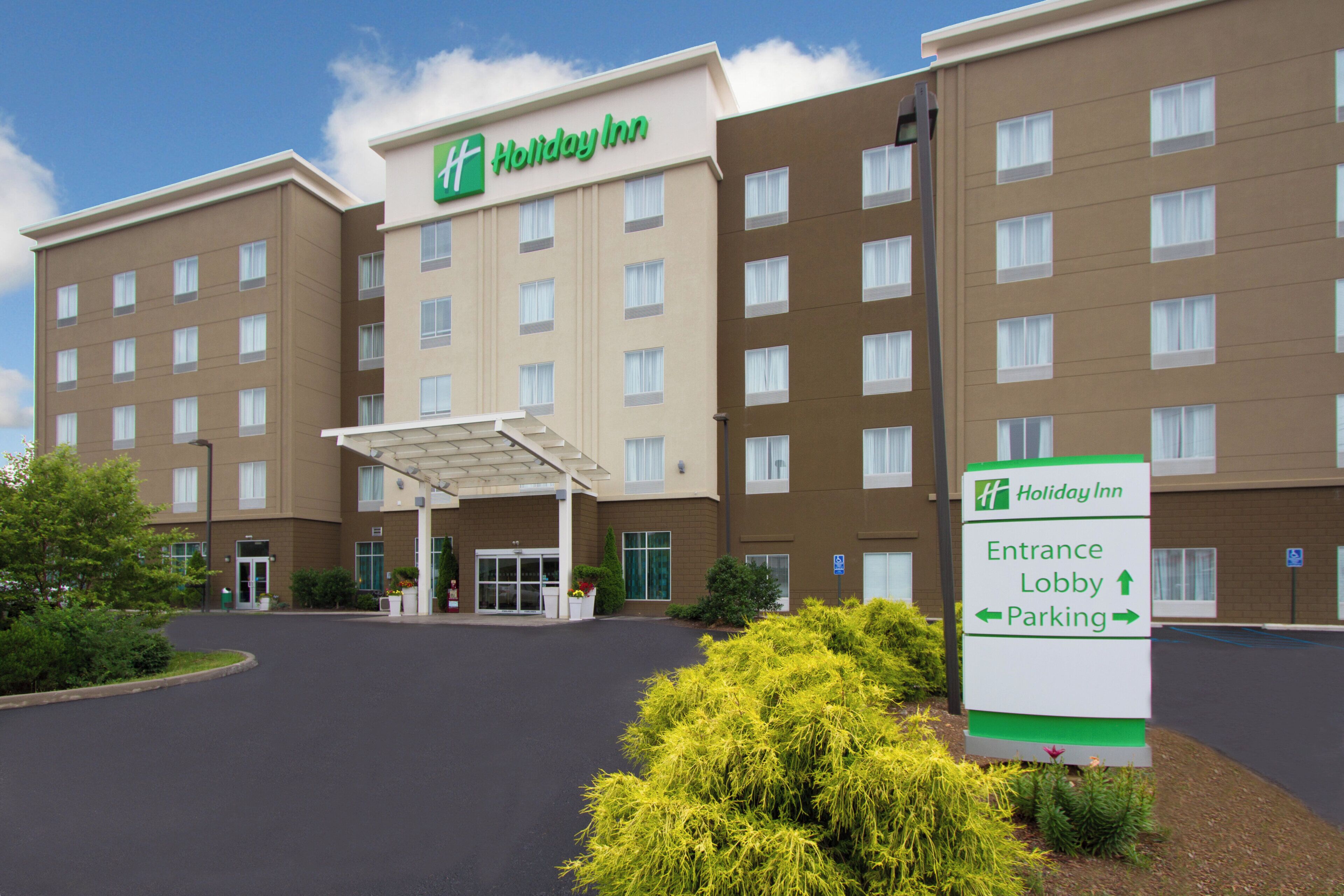 Un hôtel Holiday Inn avec une entrée bien visible, un panneau d’identification dans le hall et un panneau indiquant l’emplacement du parking.
