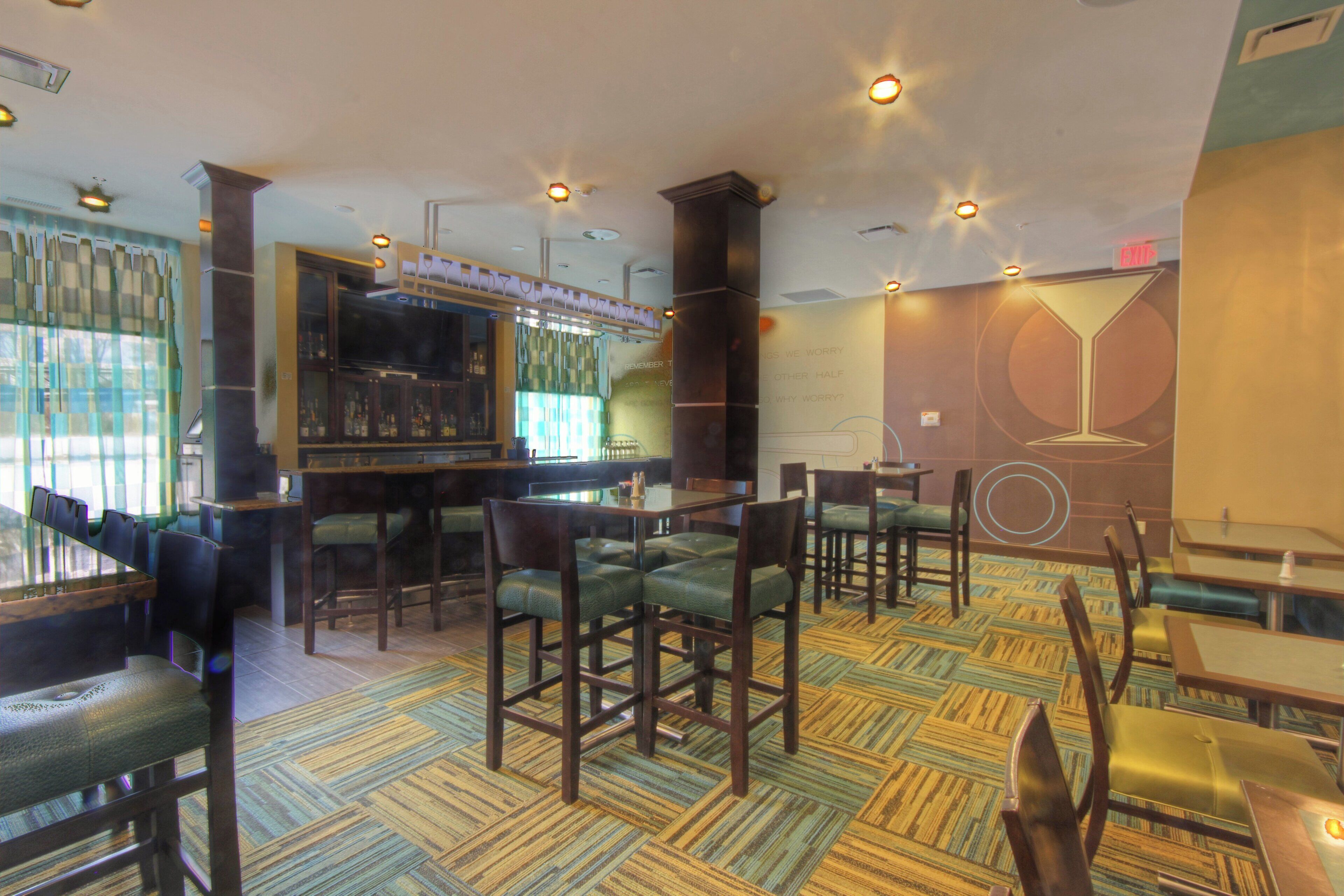 Un interior de restaurante con zona de bar, diversas disposiciones de asientos y suelo estampado.