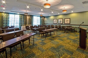 Een vergaderzaal met tafels, stoelen, een spreekgestalte en ingekaderde kunstwerken aan de muur.