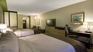 A hotel room with two beds, a desk, a television, and a desk lamp.