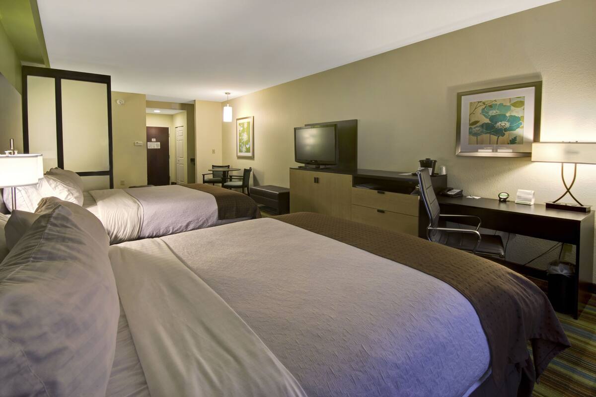 A hotel room with two beds, a desk, a television, and a desk lamp.