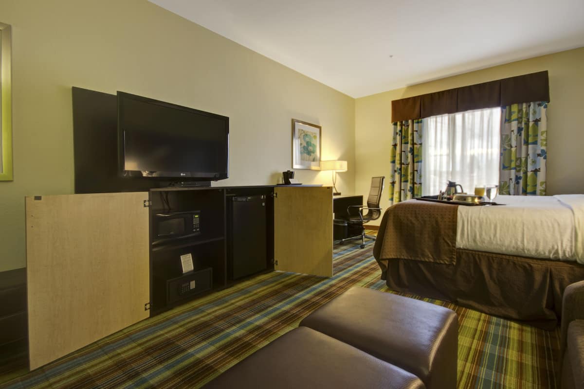 A hotel room with a bed, a TV, a desk with a computer, and a small seating area.