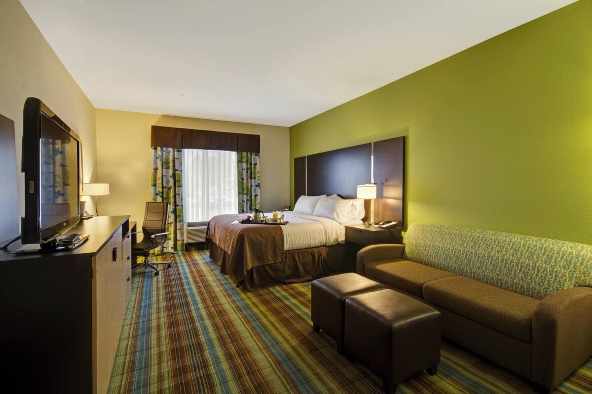 A hotel room with a bed, a desk with a computer, a sofa, and a television.