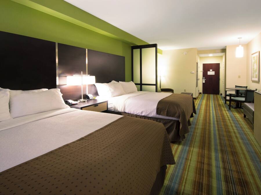 A hotel room with two beds, a desk, a chair, a television, and a door leading to another room.