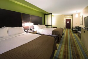 Une chambre d’hôtel avec deux lits, un bureau, une chaise, une télévision et une porte donnant sur une autre pièce.