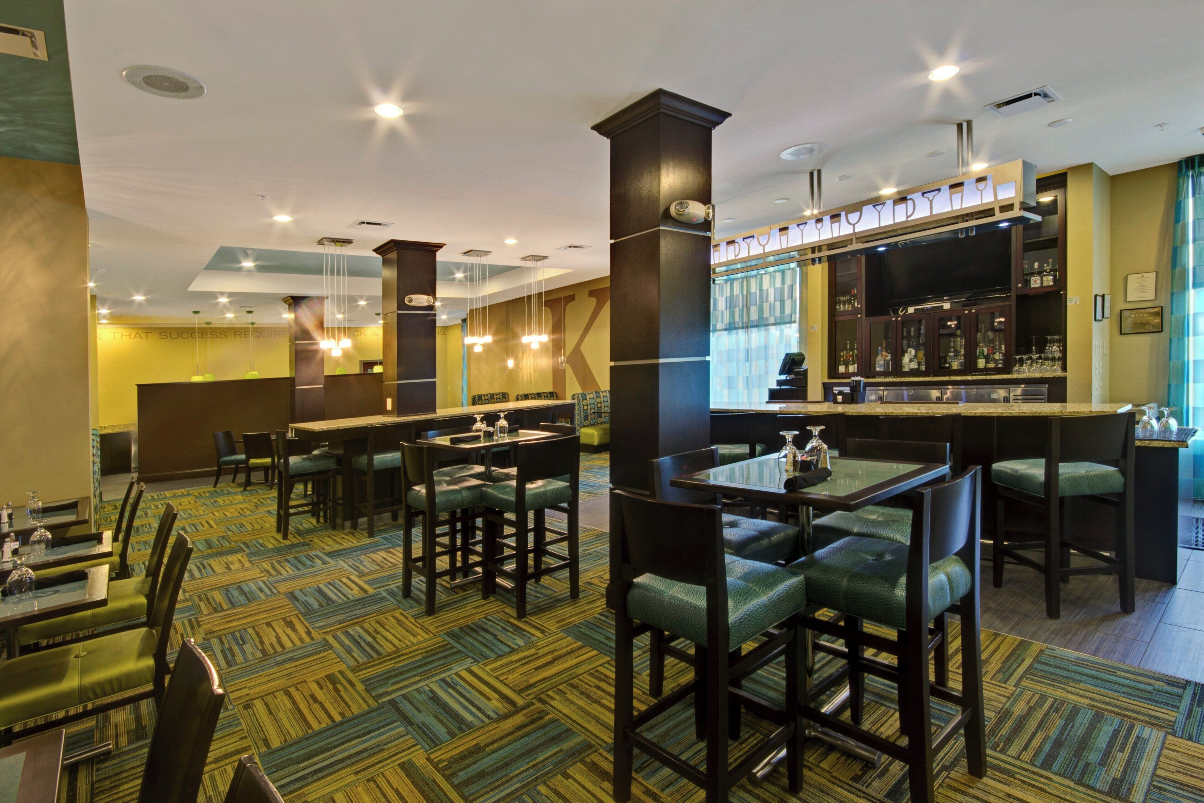Um saguão de hotel com área de bar, disposição de assentos e carpete estampado.