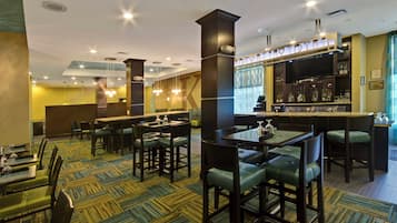 Um saguão de hotel com área de bar, disposição de assentos e carpete estampado.