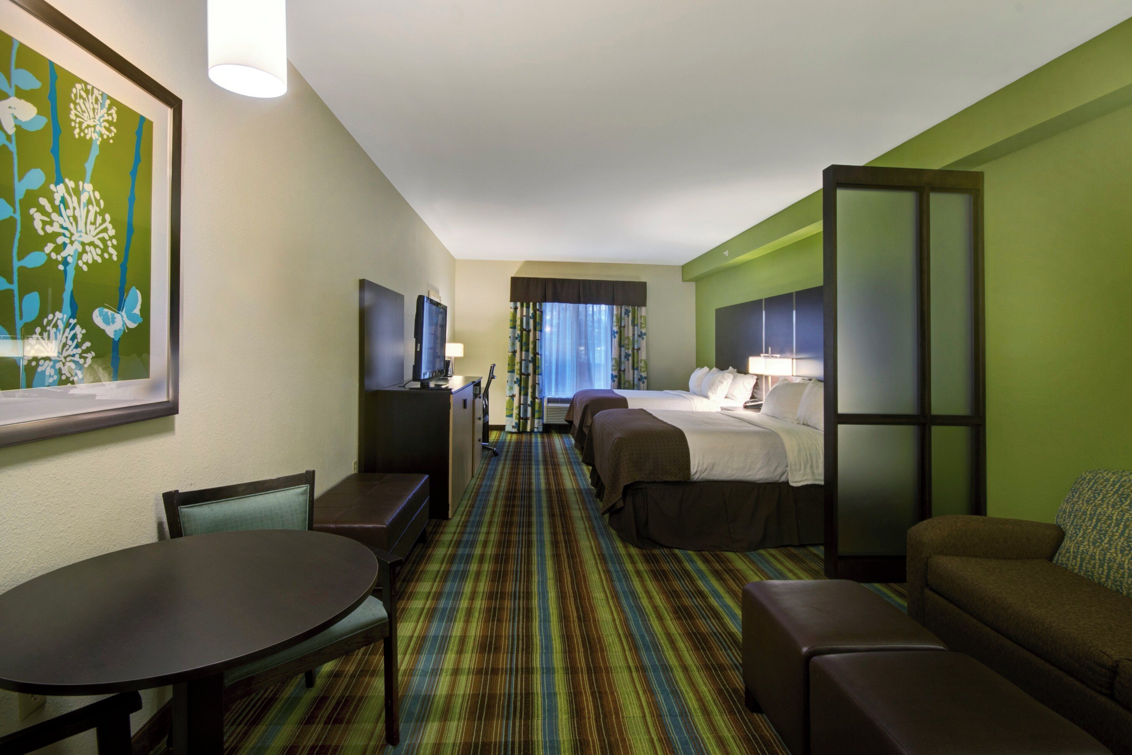 A hotel room with a bed, two bedside tables, a desk, a chair, a sofa, and a television.