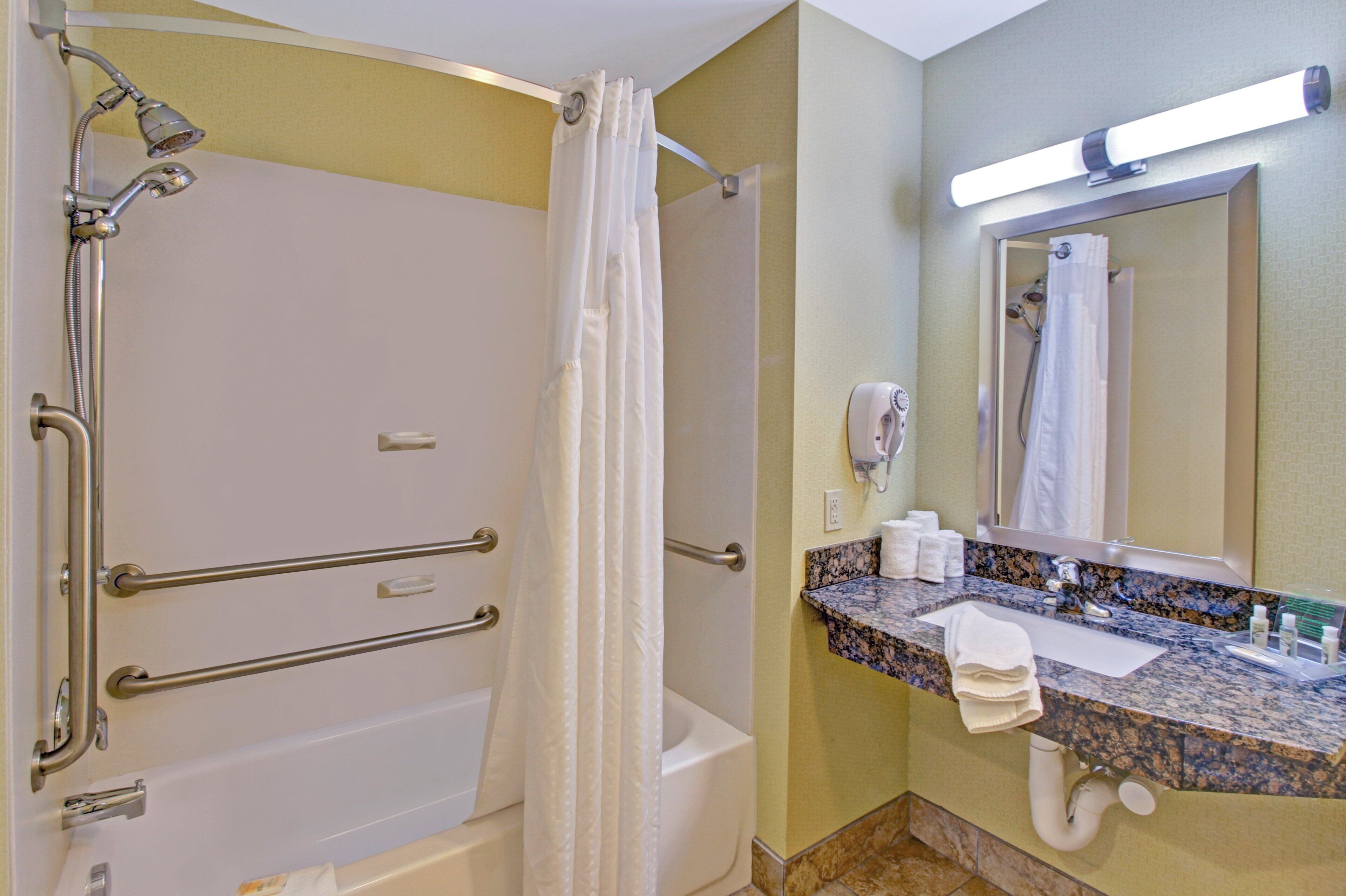 A bathroom with a walk-in shower, grab bars, a toilet, a sink with a mirror, and a towel rack.