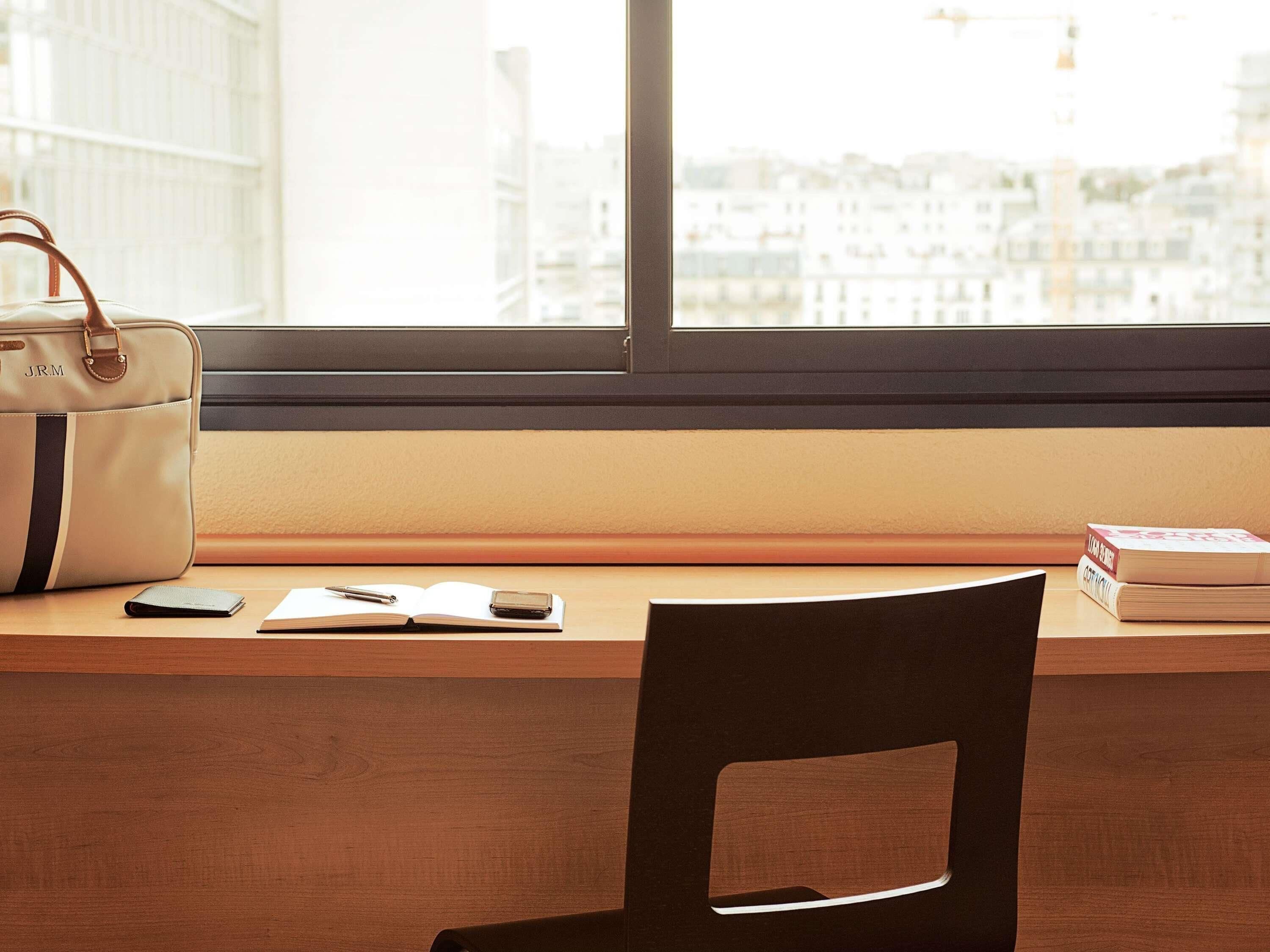 A desk with a leather bag, a notebook, a pen, a smartphone, and books.