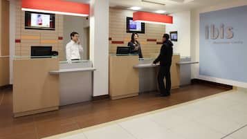 A reception area with a modern design, featuring a glass counter, a digital screen, and a sign indicating the location as 'ibis Manchester Centre'.