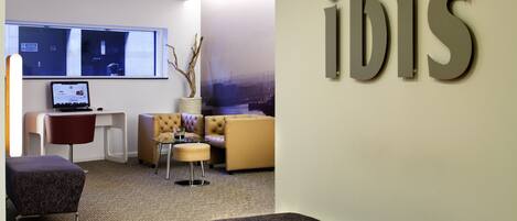 A modern hotel lobby with a seating area, a desk, and a large window.