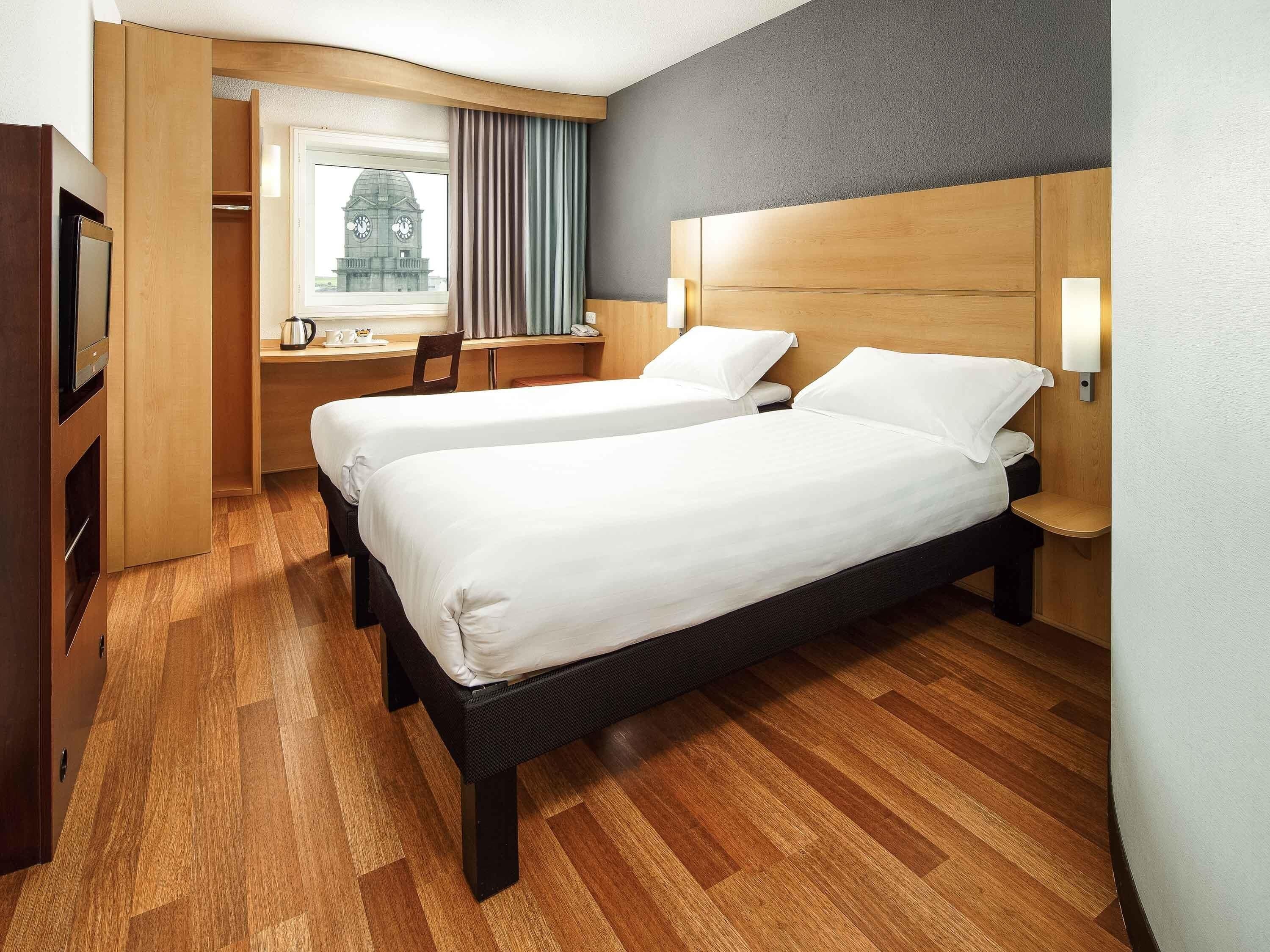Une chambre d’hôtel avec deux lits, un bureau, une chaise, une télévision et une fenêtre donnant sur un beffroi.