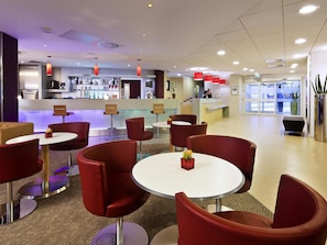 Eine Hotelhalle mit roten Stühlen, einer Rezeption und einem Barbereich.