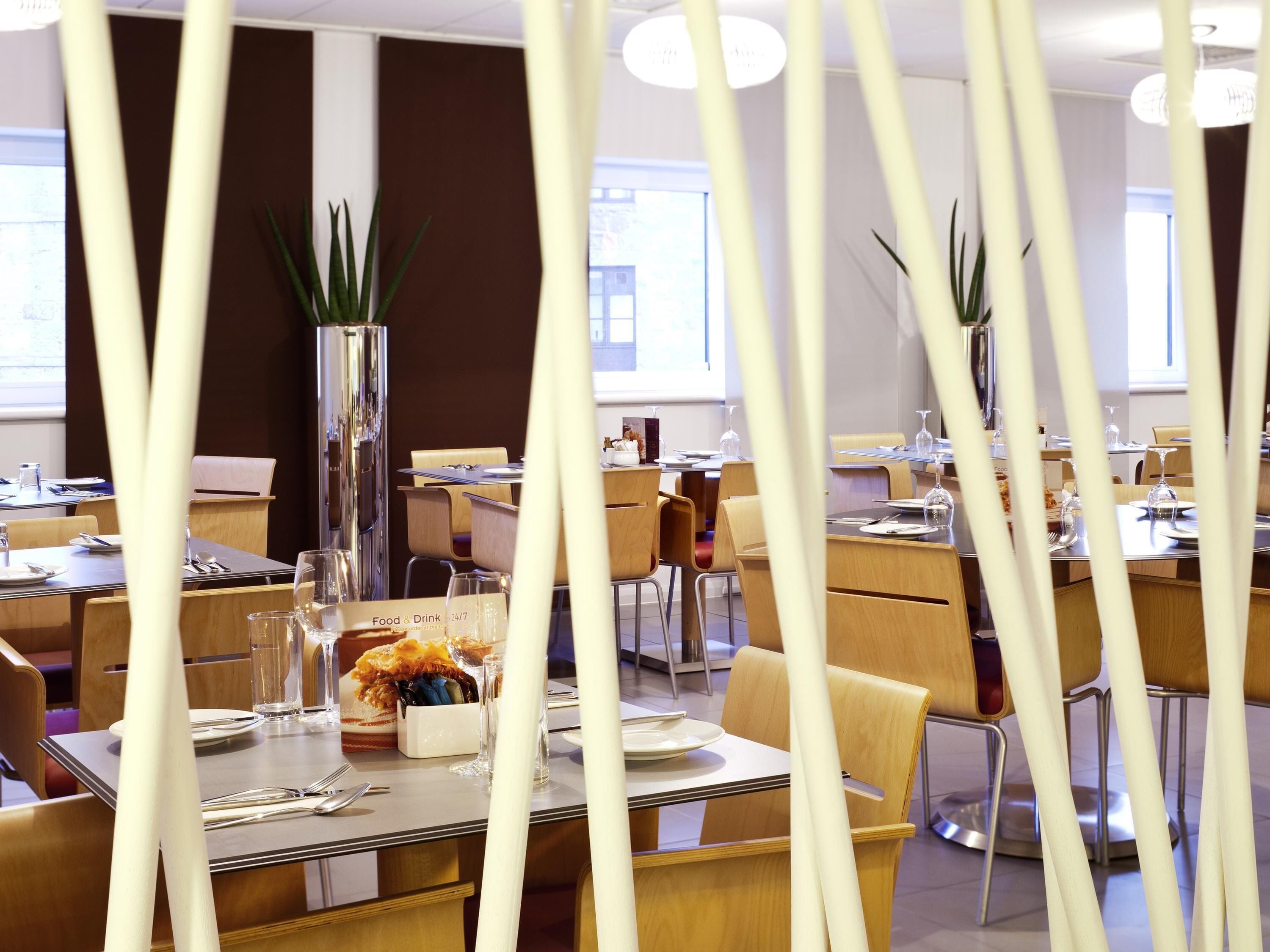A restaurant with tables set for dining, chairs, and a large vase with plants.