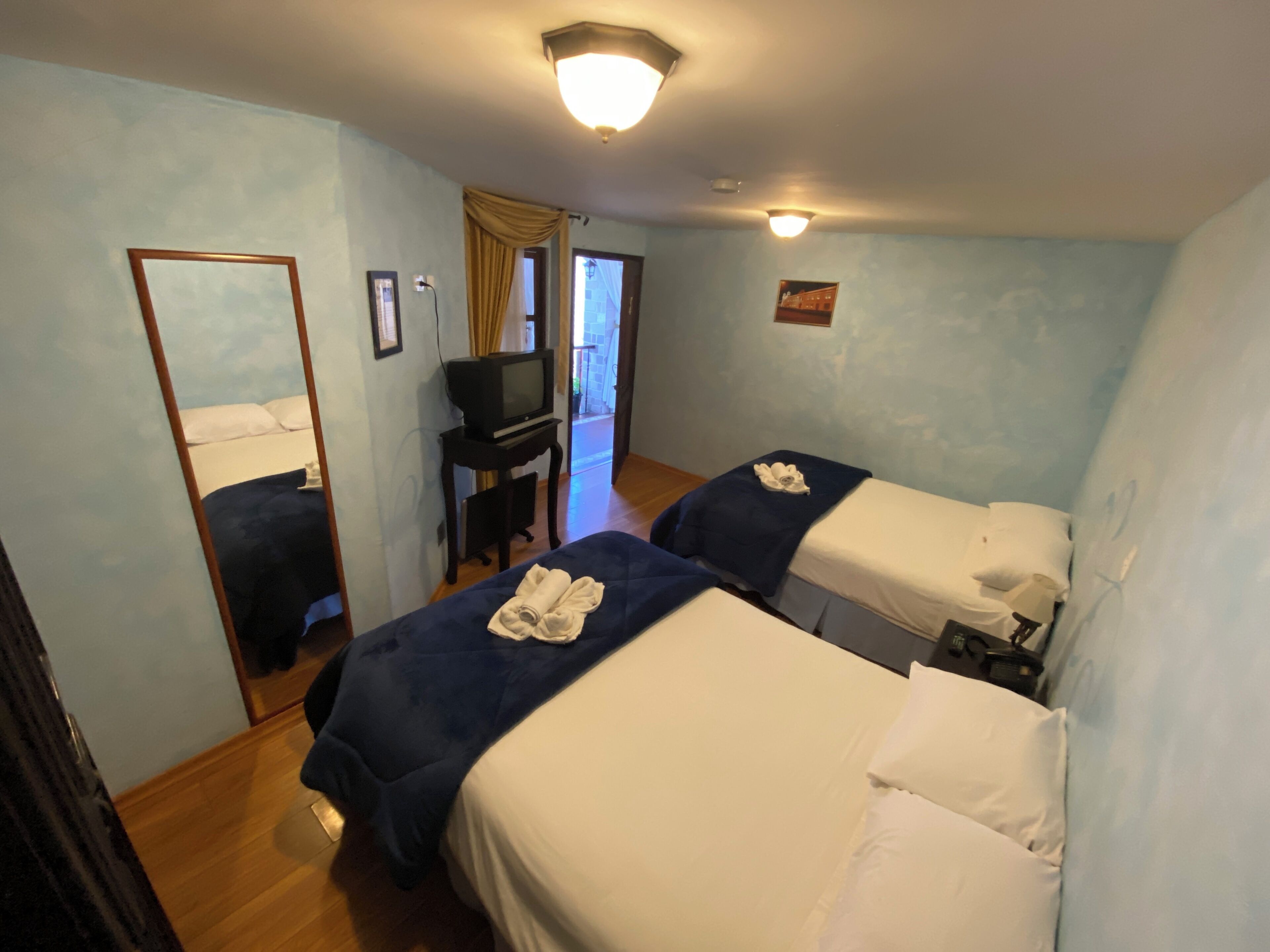 A hotel room with two beds, a desk with a television, and a mirror.