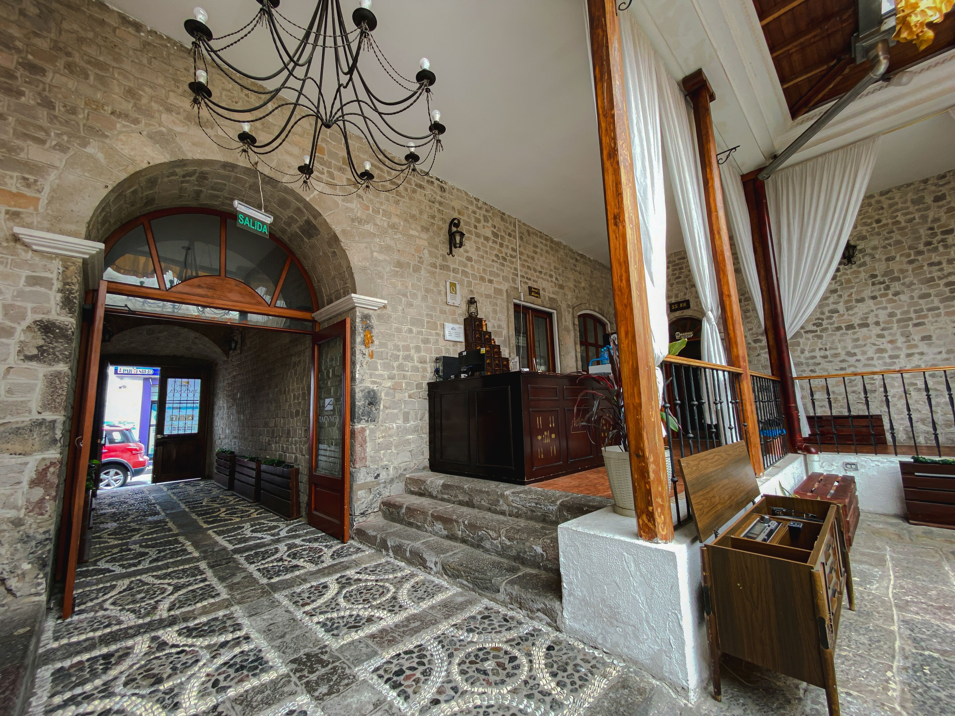 A lobby with a stone wall, a chandelier, a staircase, and a reception desk.