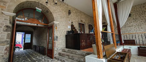 A lobby with a stone wall, a chandelier, a staircase, and a reception desk.