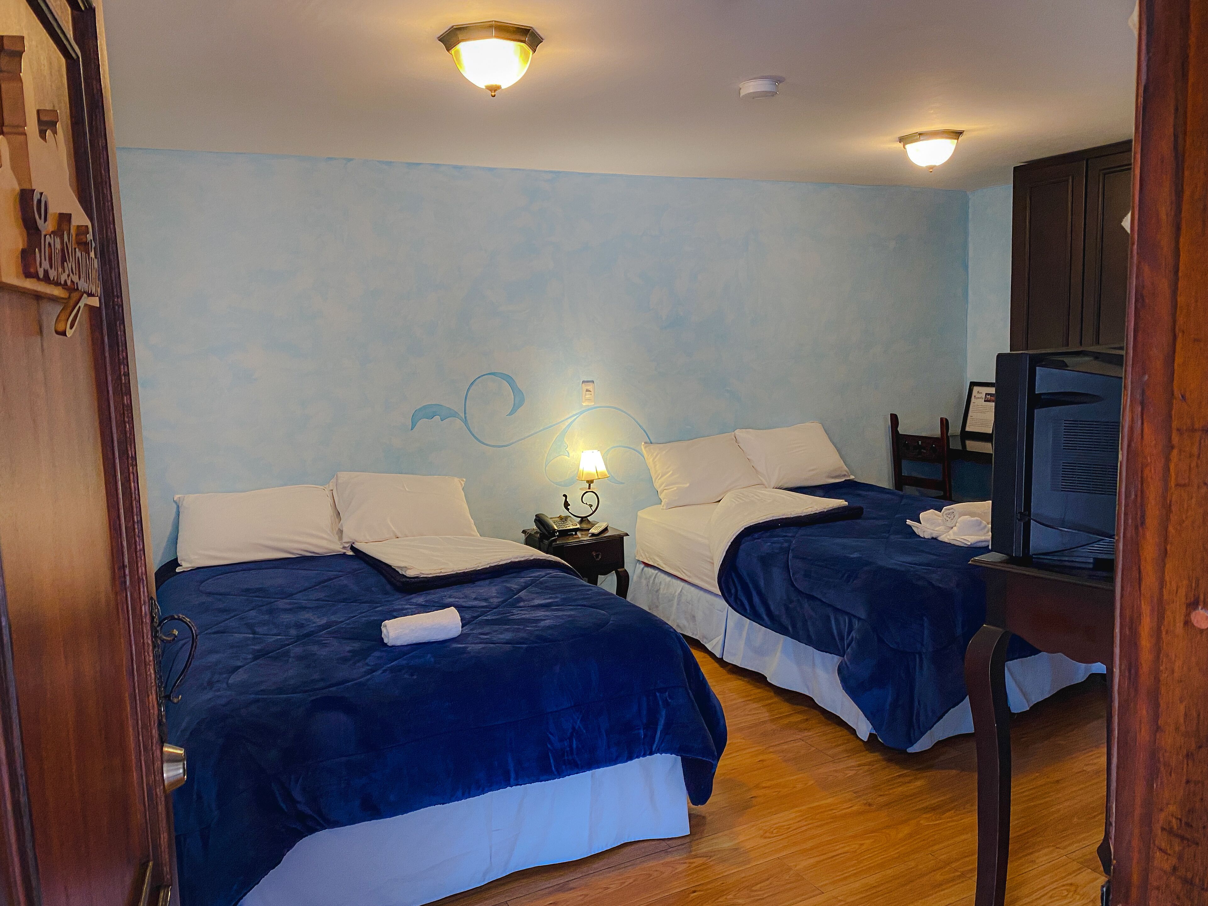 Habitación de hotel con dos camas, una televisión y una mesita de noche con lámpara.