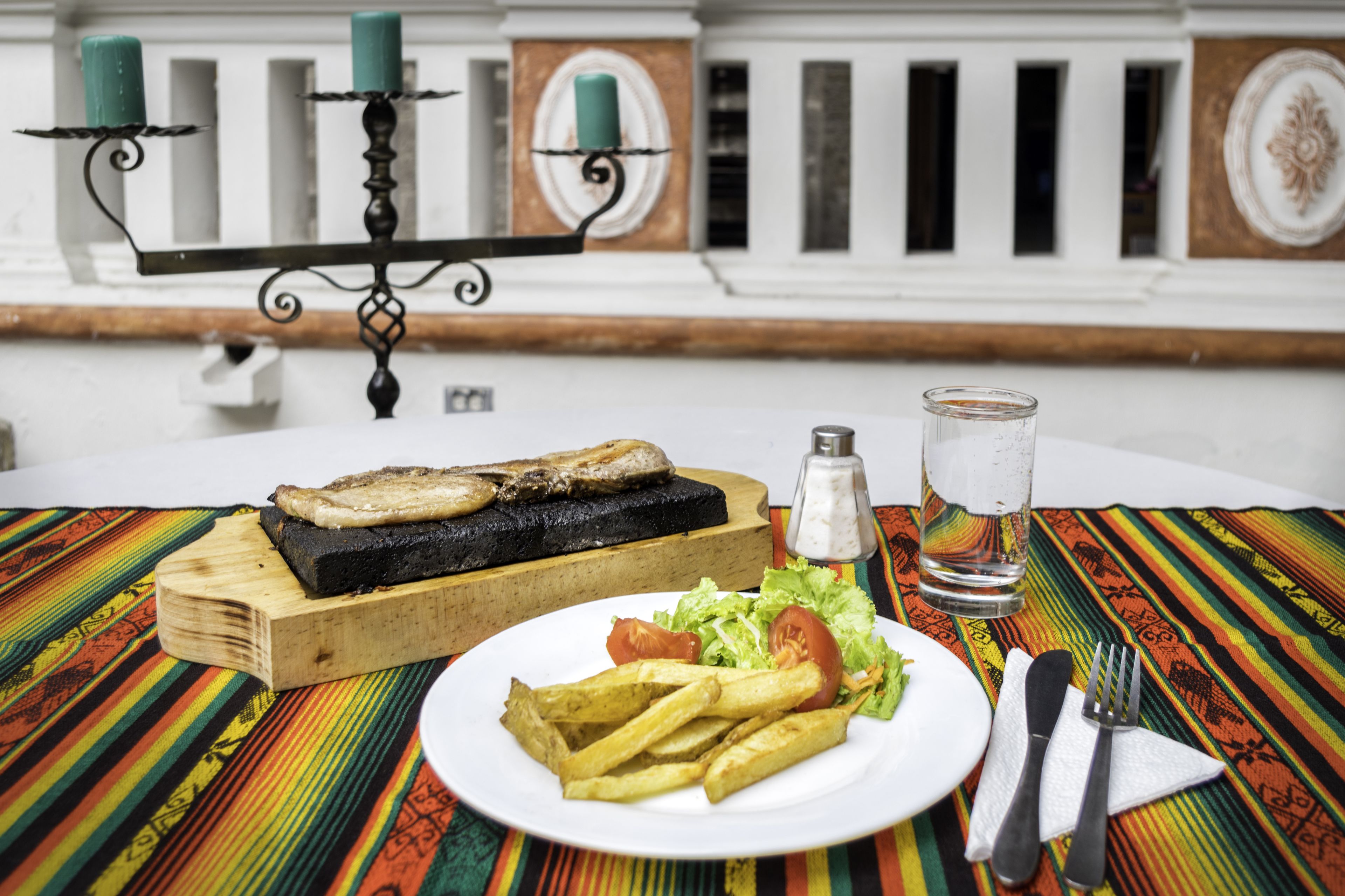 Una mesa de comedor con un plato de comida, un vaso de agua y saleros y pimenteros.