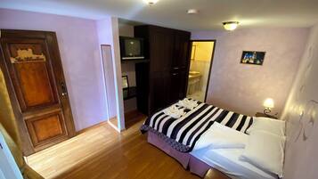 A hotel room with a bed, wooden flooring, a television, a wardrobe, and a bathroom visible through an open door.