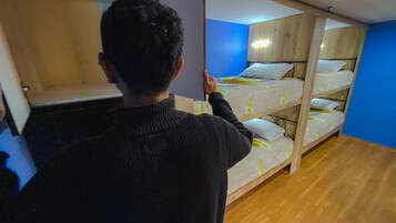 Une personne ouvre une porte coulissante donnant sur une pièce où se trouvent des lits superposés.