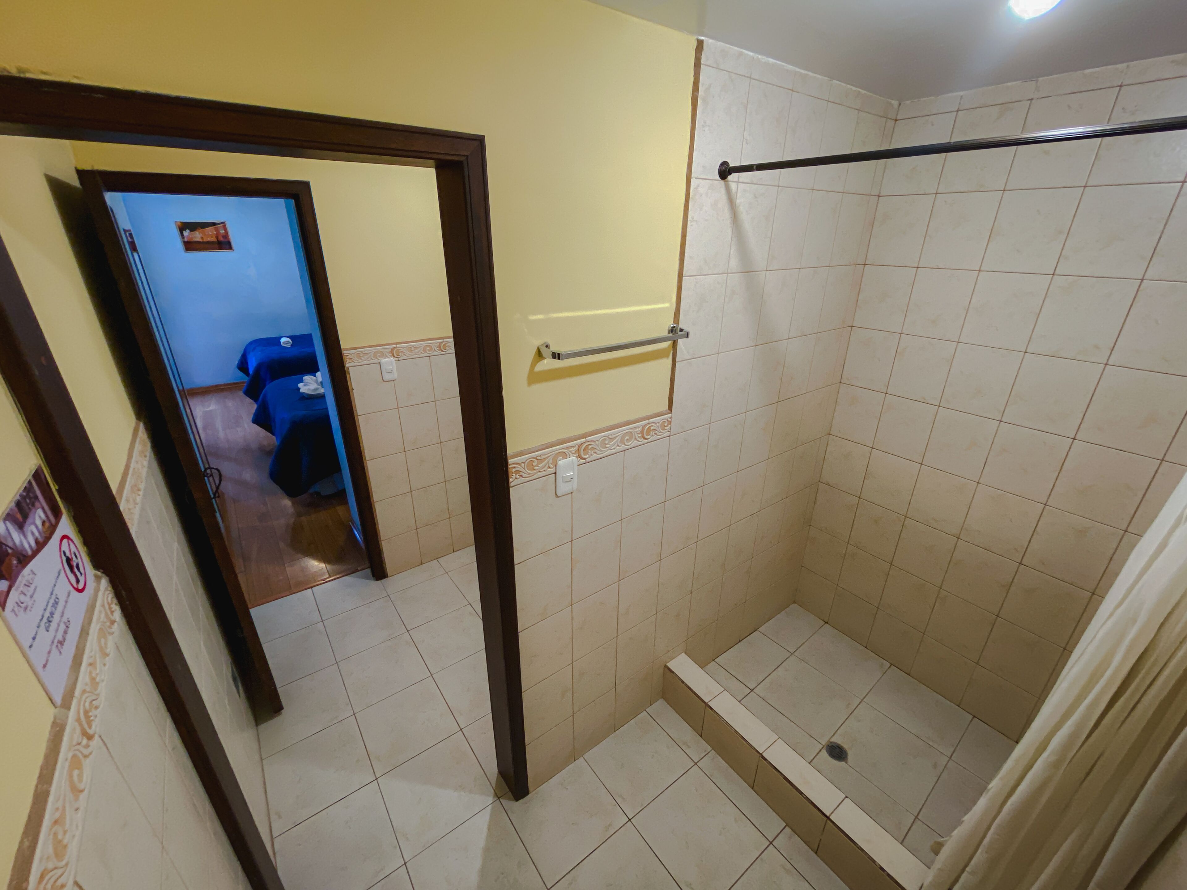 A bathroom with a shower, tiled walls, a towel rack, and a door leading to another room.