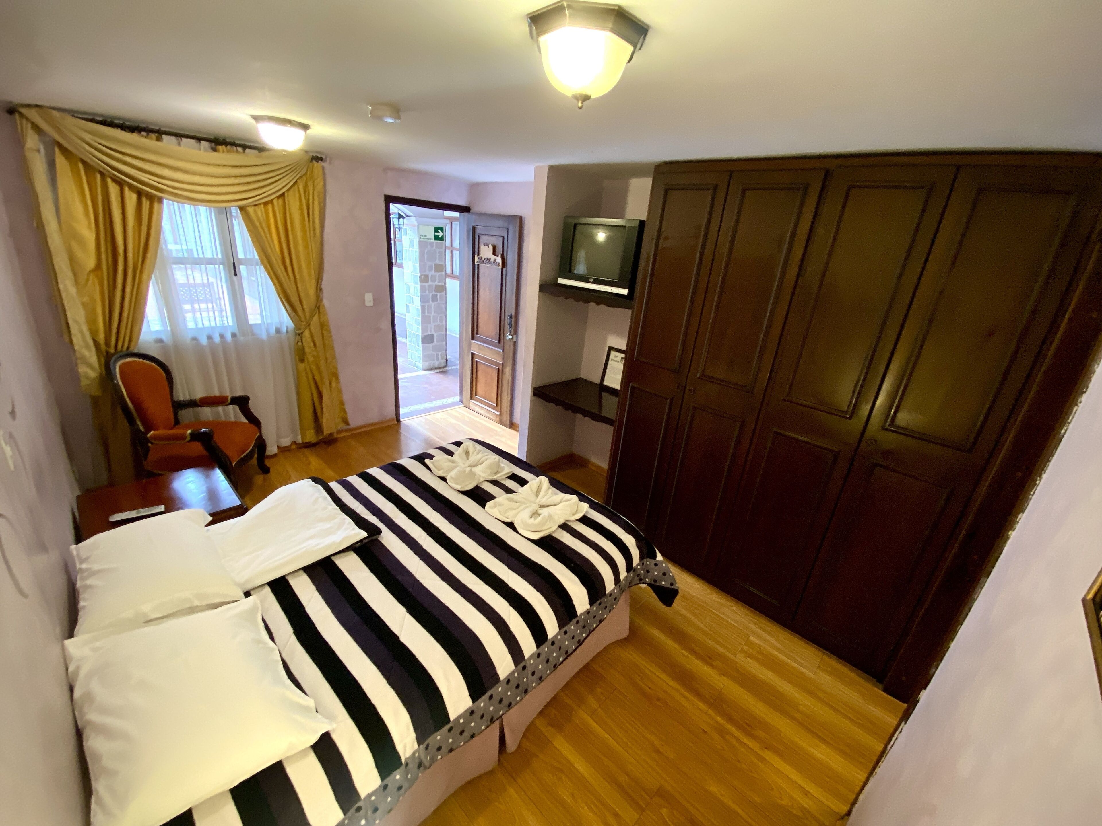 A hotel room with a bed, a chair, a TV, and a wardrobe.