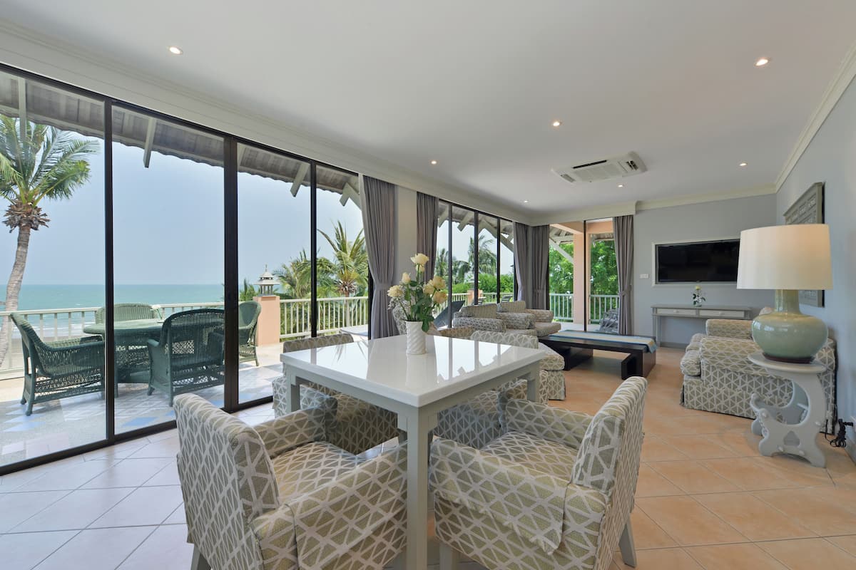 Een ruime woonkamer met balkon en uitzicht op zee, ingericht met gestreepte banken en een eettafel.