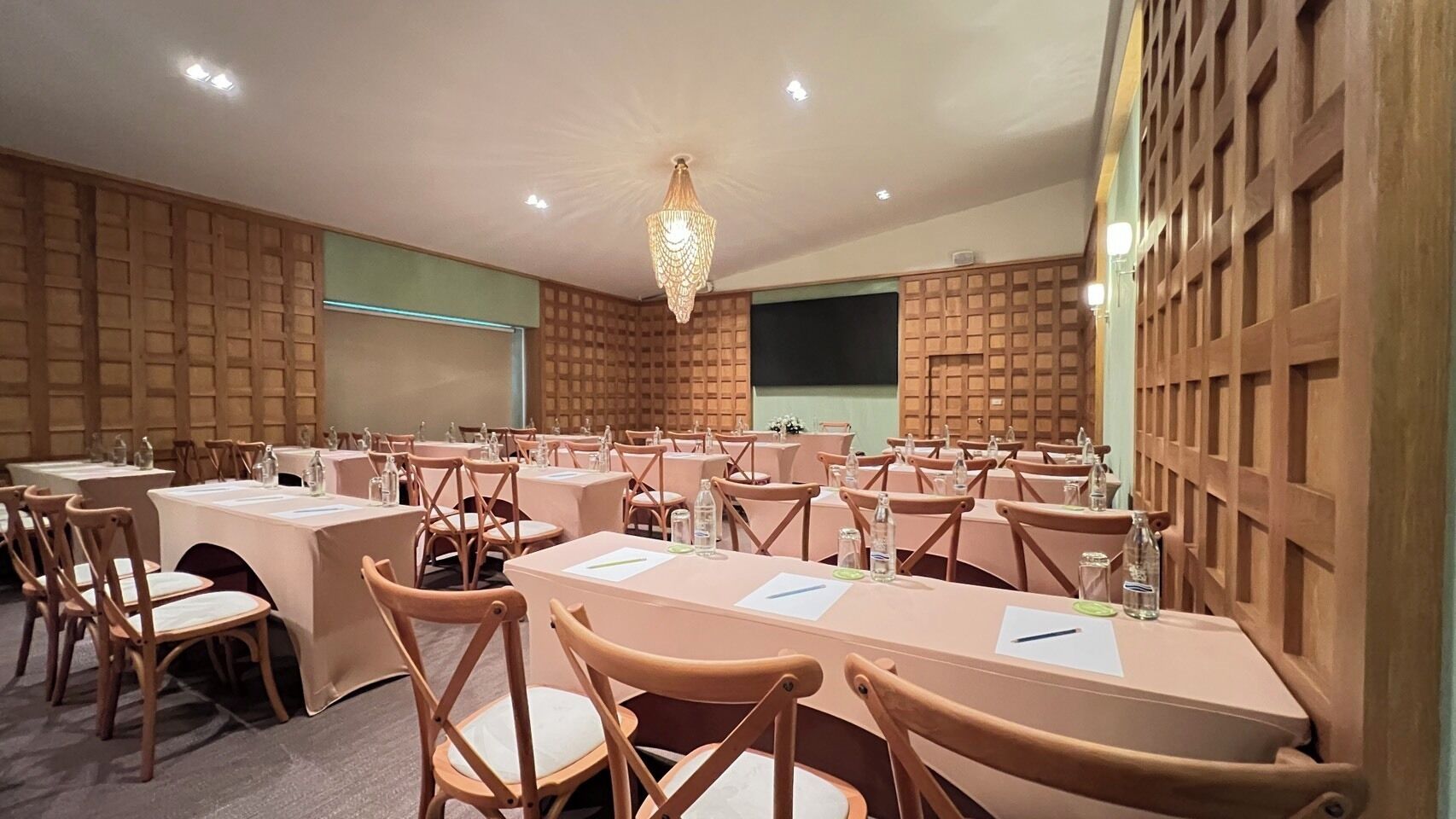 Une salle de conférence dotée de plusieurs tables et chaises, équipée de bouteilles d’eau et de documents, ainsi que d’un écran de projection fixé au mur.