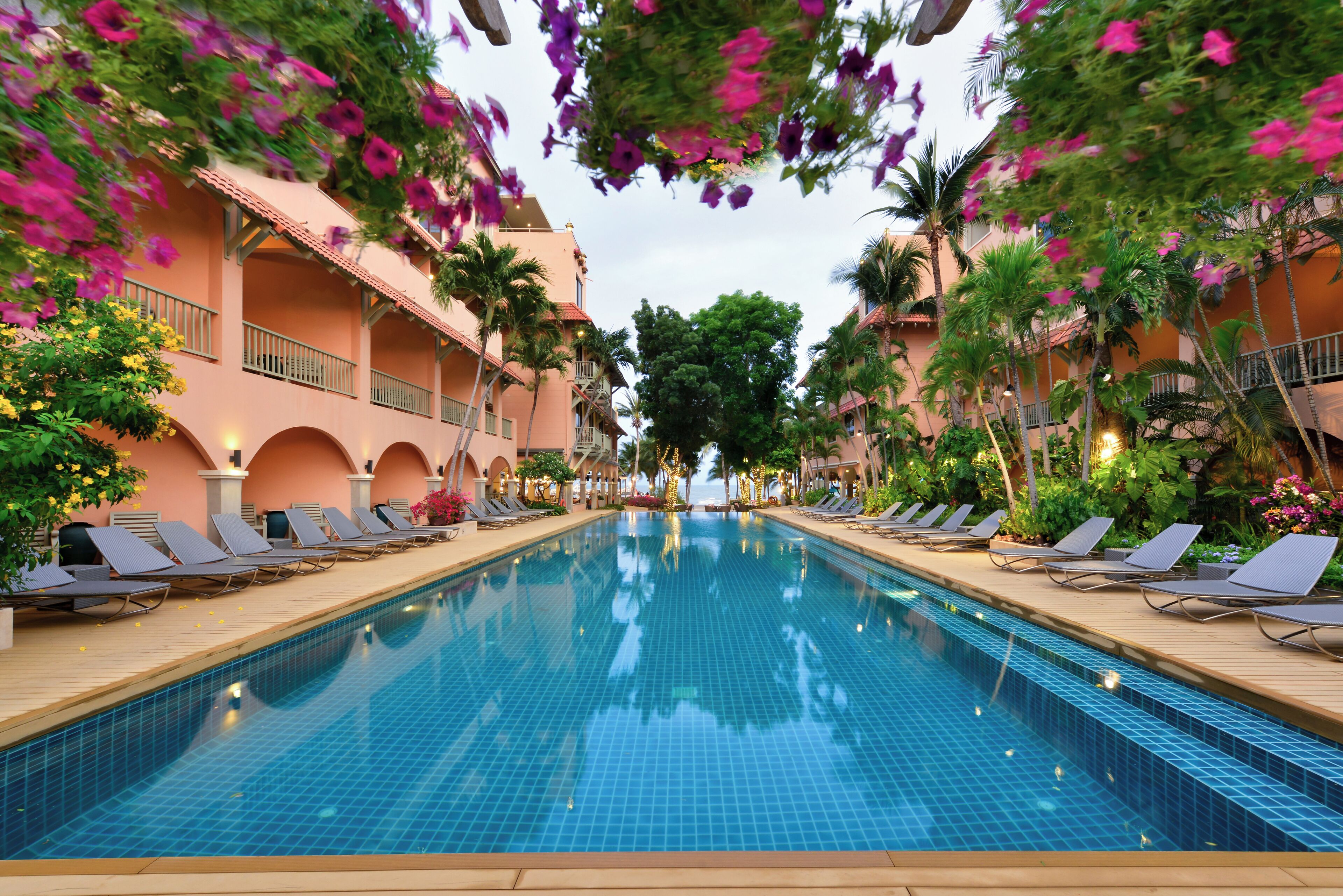 A swimming pool with lounge chairs and a building with balconies.