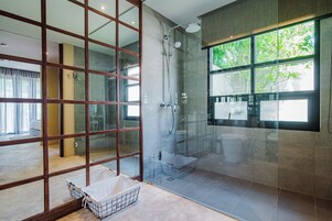 Un baño moderno con cabina de ducha de vidrio, un ventanal con vistas a la vegetación y una separación de madera.