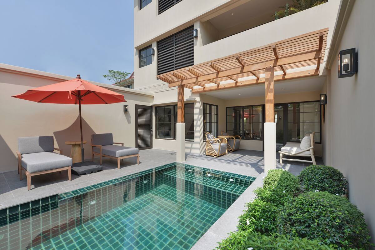 Een modern buitenzwembad met een pergola, ligbedden en een rode parasol.