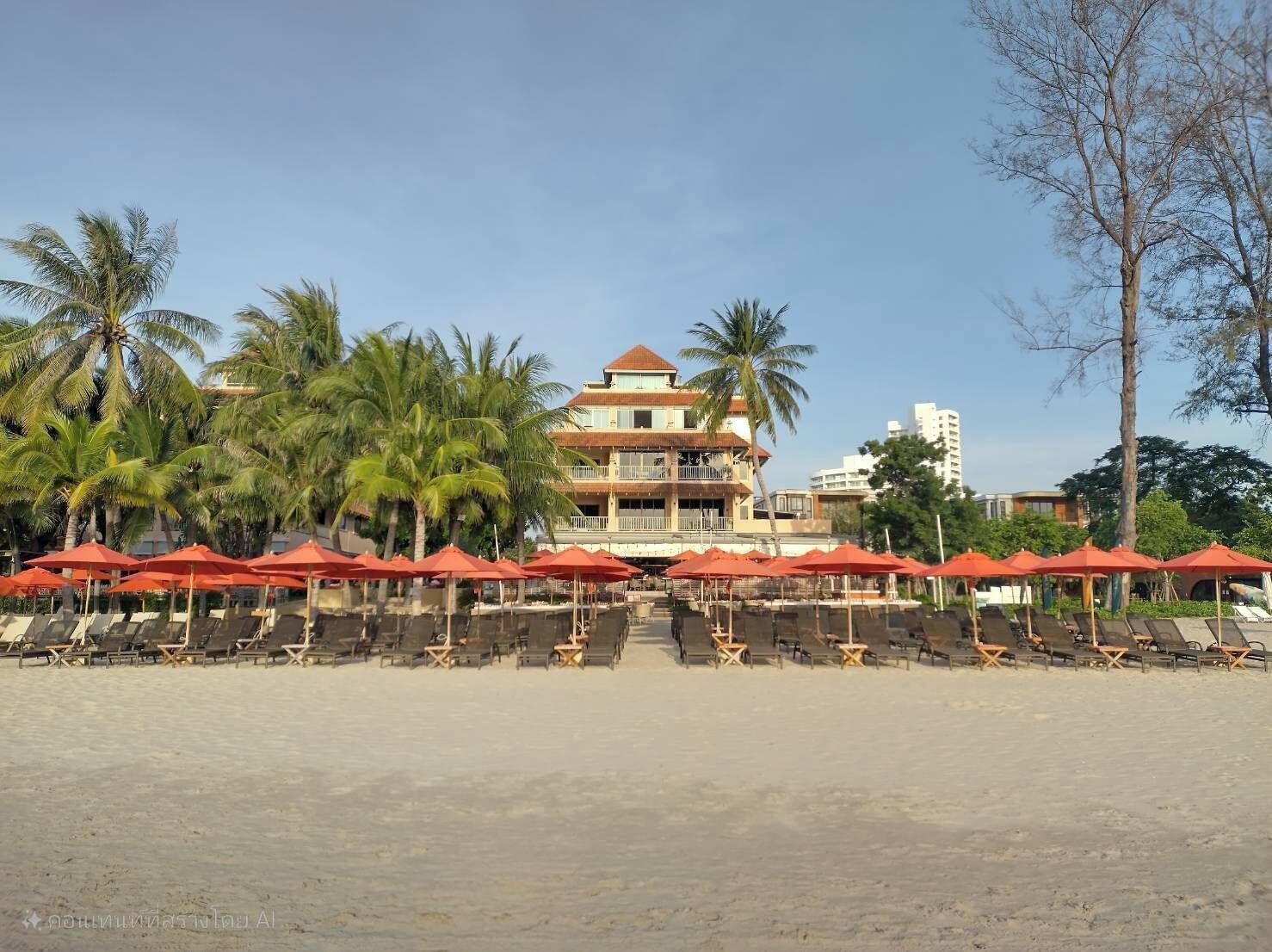 A beachside hotel with multiple red umbrellas and sun loungers, palm trees, and a two-story building with balconies.