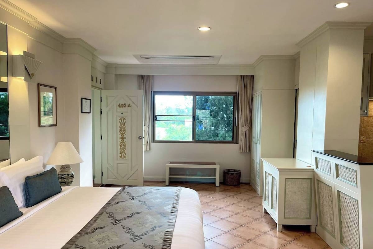 Een hotelkamer met een groot bed, een bureau, een raam met gordijnen en uitzicht op groen.