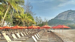 A beach with rows of sun loungers and red umbrellas, palm trees, and a mountainous backdrop. - Anantasila Beach Resort Hua Hin (Hua Hin)