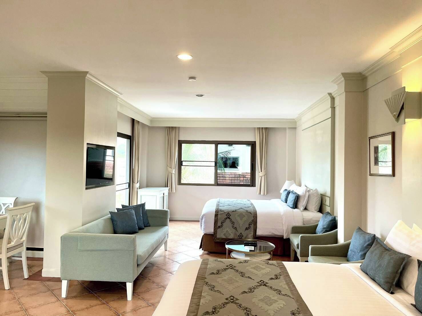 A hotel room with a bed, a sofa, a television, a desk, and a window with a view of the outside.