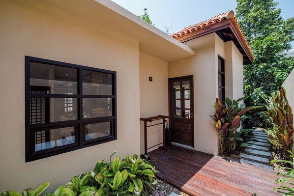 A modern house with a large window, a wooden door, and a small porch area with plants.