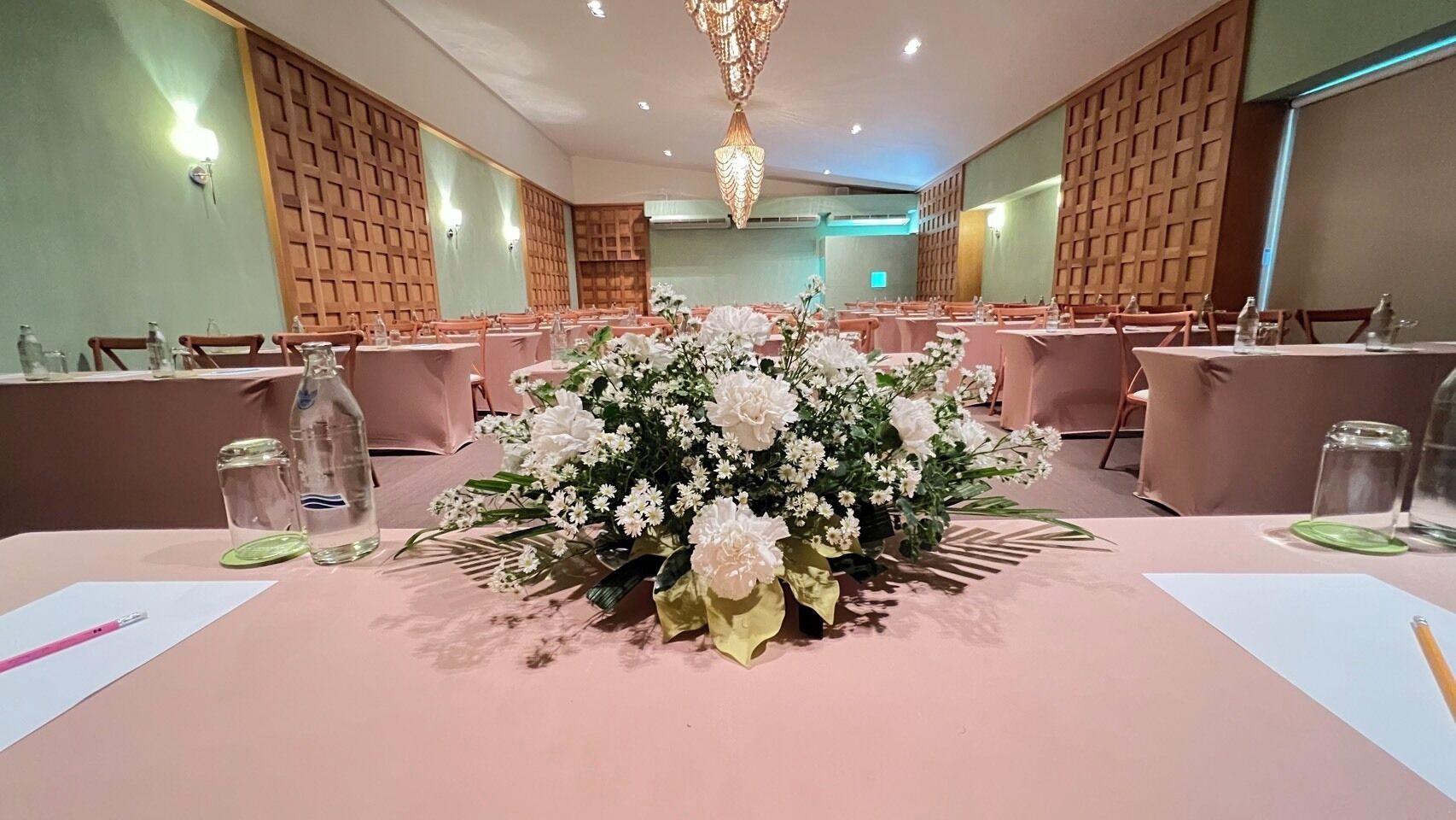 A conference room with tables set for a meeting, featuring floral centerpieces and water bottles.