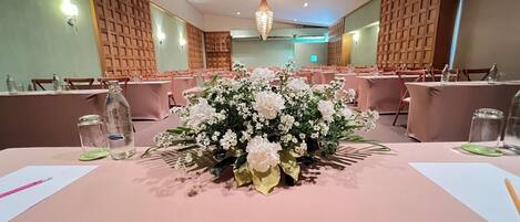 A conference room with tables set for a meeting, featuring floral centerpieces and water bottles.
