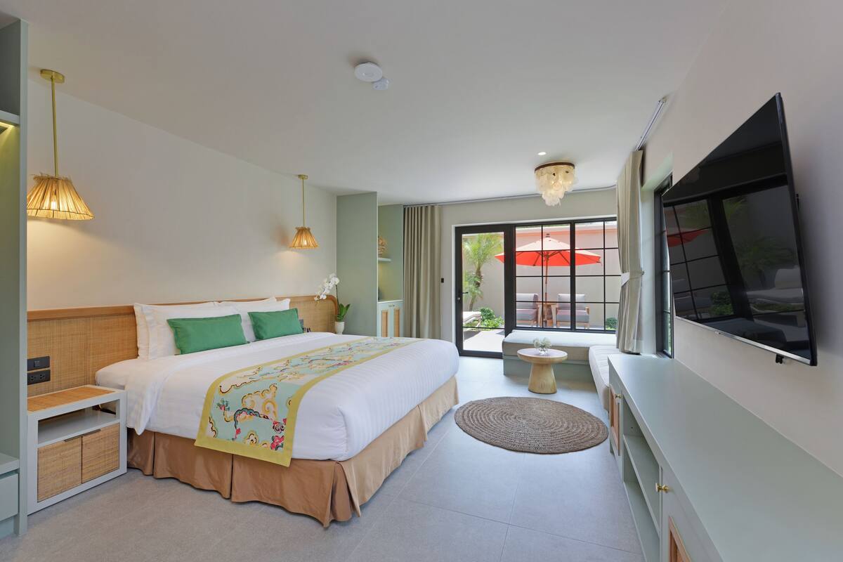 Een moderne hotelkamer met een groot bed, nachtkastjes, een televisie en een balkon met een parasol.